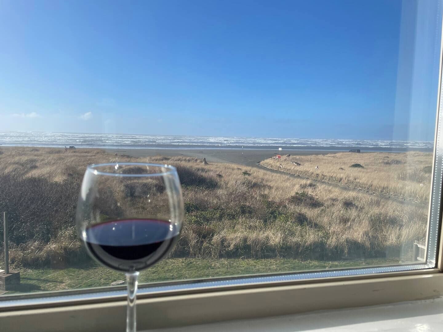 A window with a view of a beach and a glass of red wine.