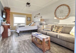 A cozy living room with a bed, a sofa, a coffee table, and a large window.