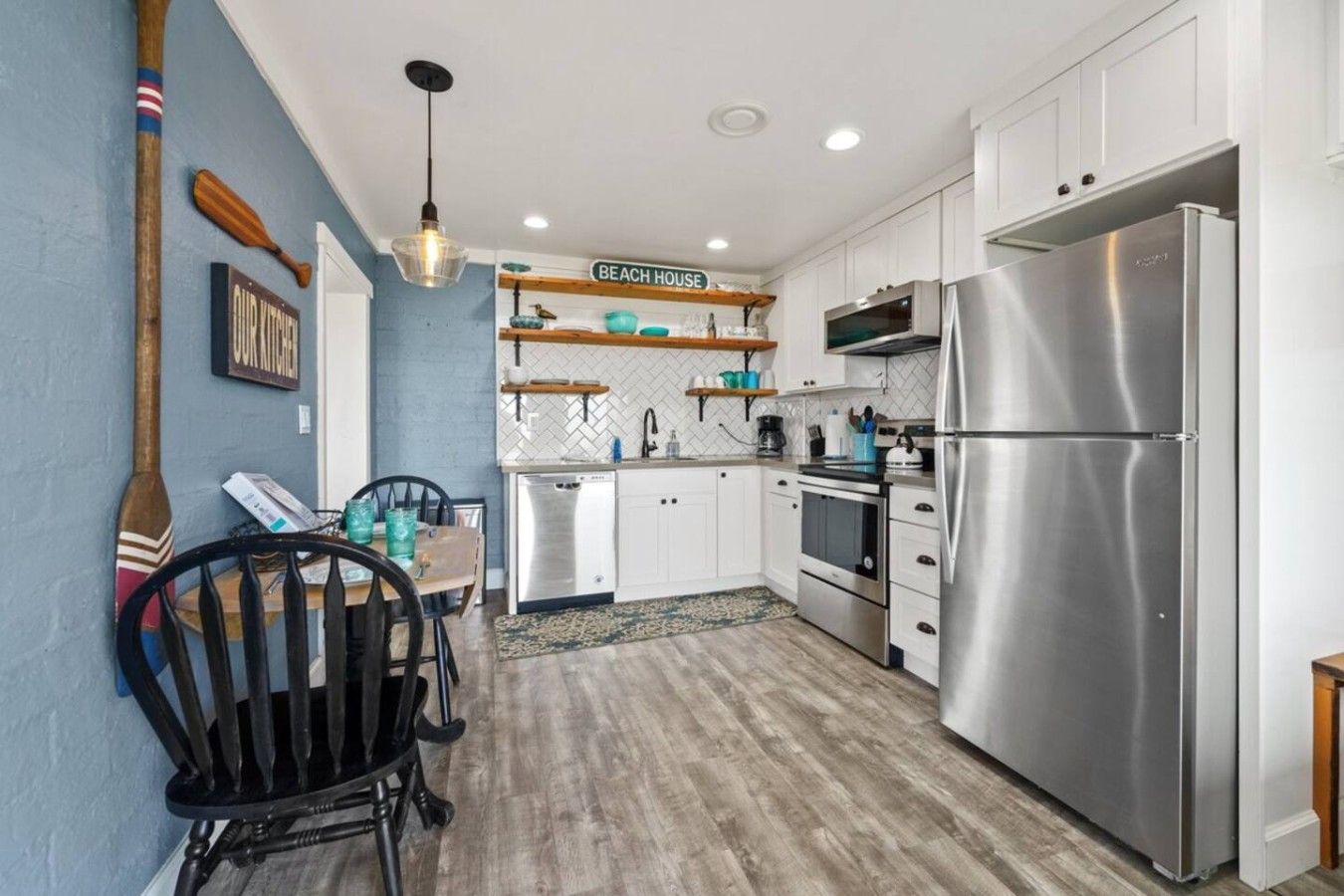 A modern kitchen with white cabinets, a stainless steel refrigerator, and a wooden dining table with chairs.