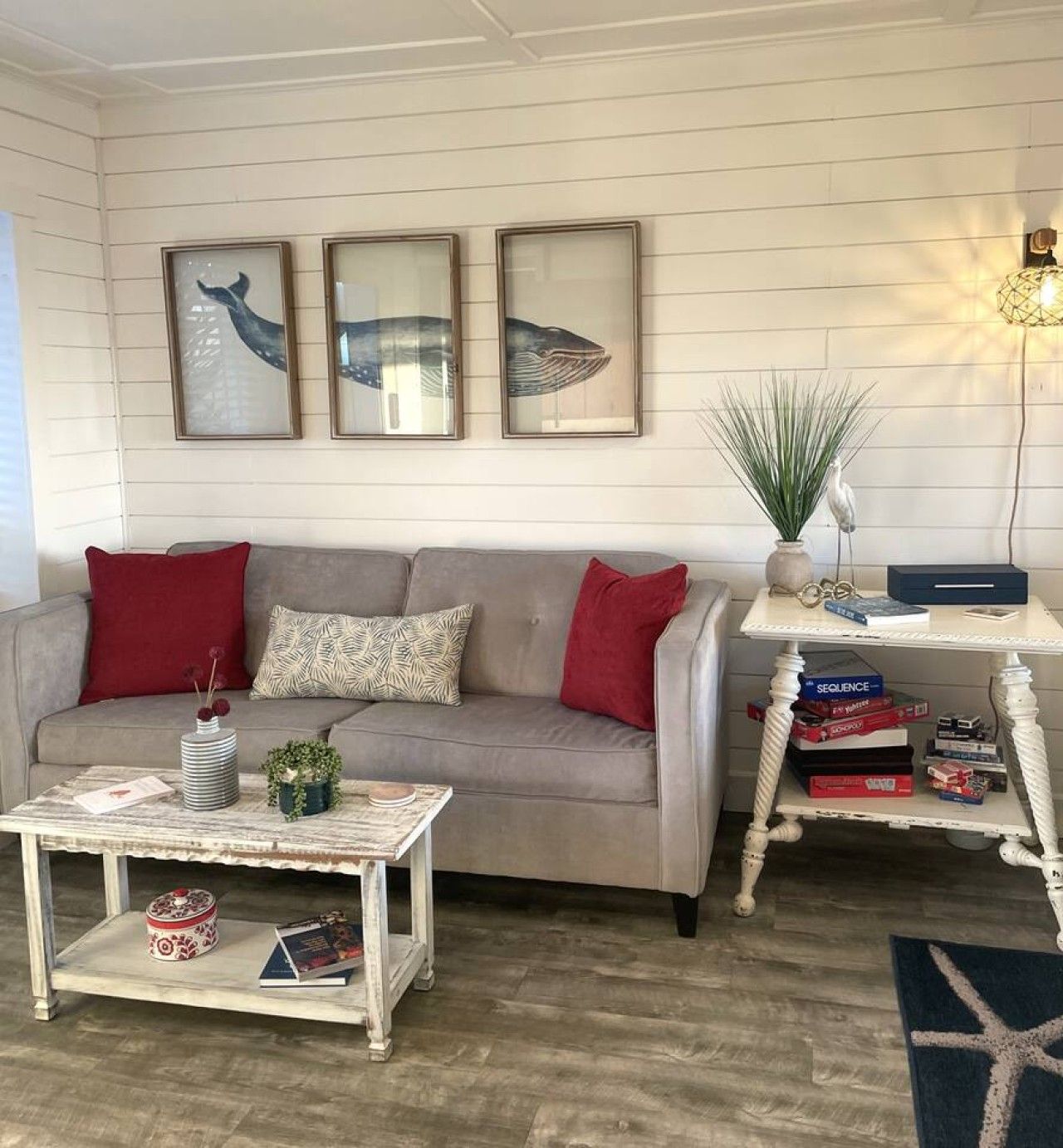 A living room with a grey sofa, red cushions, a white coffee table with books, and framed artwork on the wall.