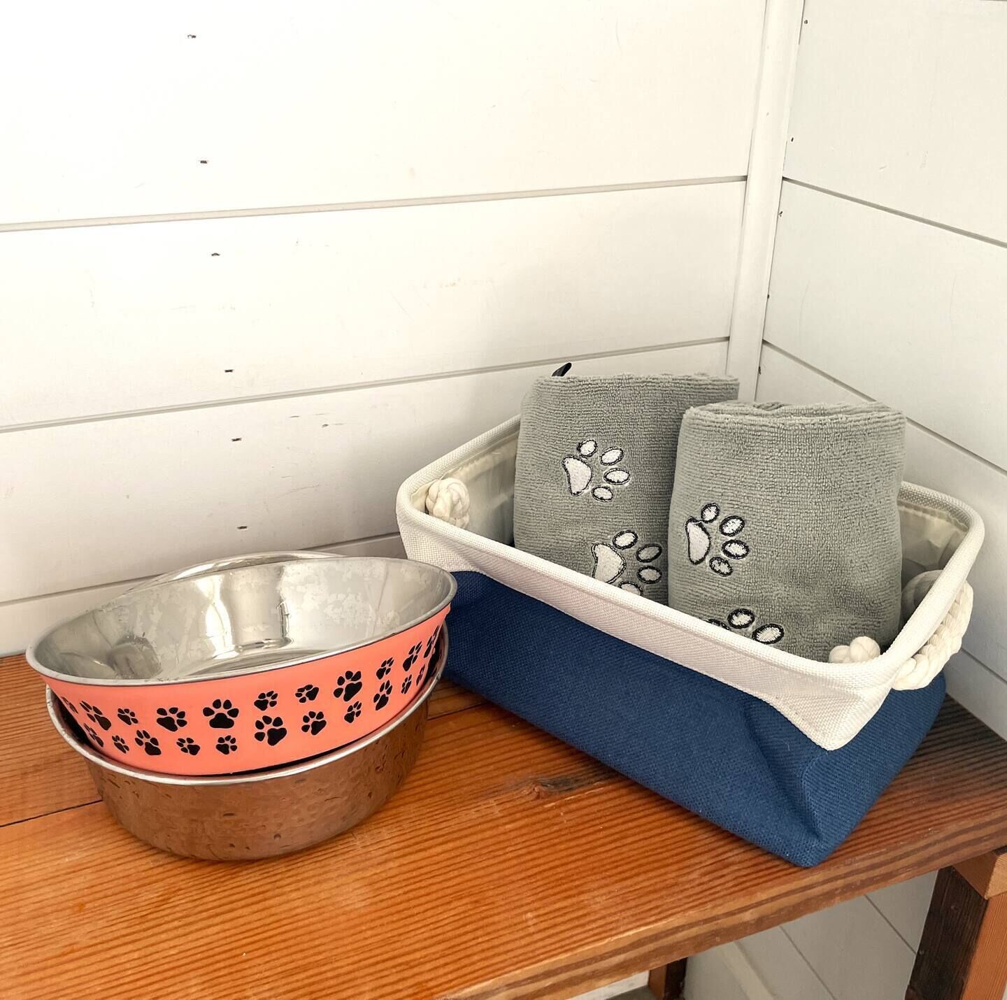 Un bol en métal orné d’empreintes de pattes, un panier bleu et blanc avec des motifs d’empreintes de pattes de chien, et une table en bois.
