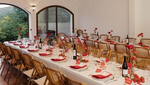 A long dining table set with red napkins, glassware, and wicker chairs in a room with wooden beams and large windows. - nowenqew;PIHFR' (Cunit)