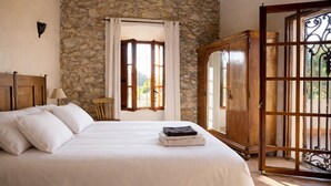 A bedroom with a stone wall, a bed with white linens, a wooden wardrobe, and a window with curtains. - nowenqew;PIHFR' (Cunit)