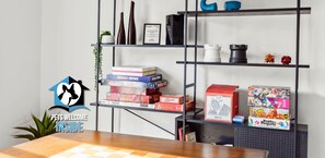 A room with a wooden table, a bookshelf with board games, and a 'Pets Welcome Inside' sign.