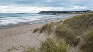 A beach with sand and grass, a person walking, and houses in the background. - Sea Breeze Apt 2 - 2 Bed - Horton Beach (Swansea)