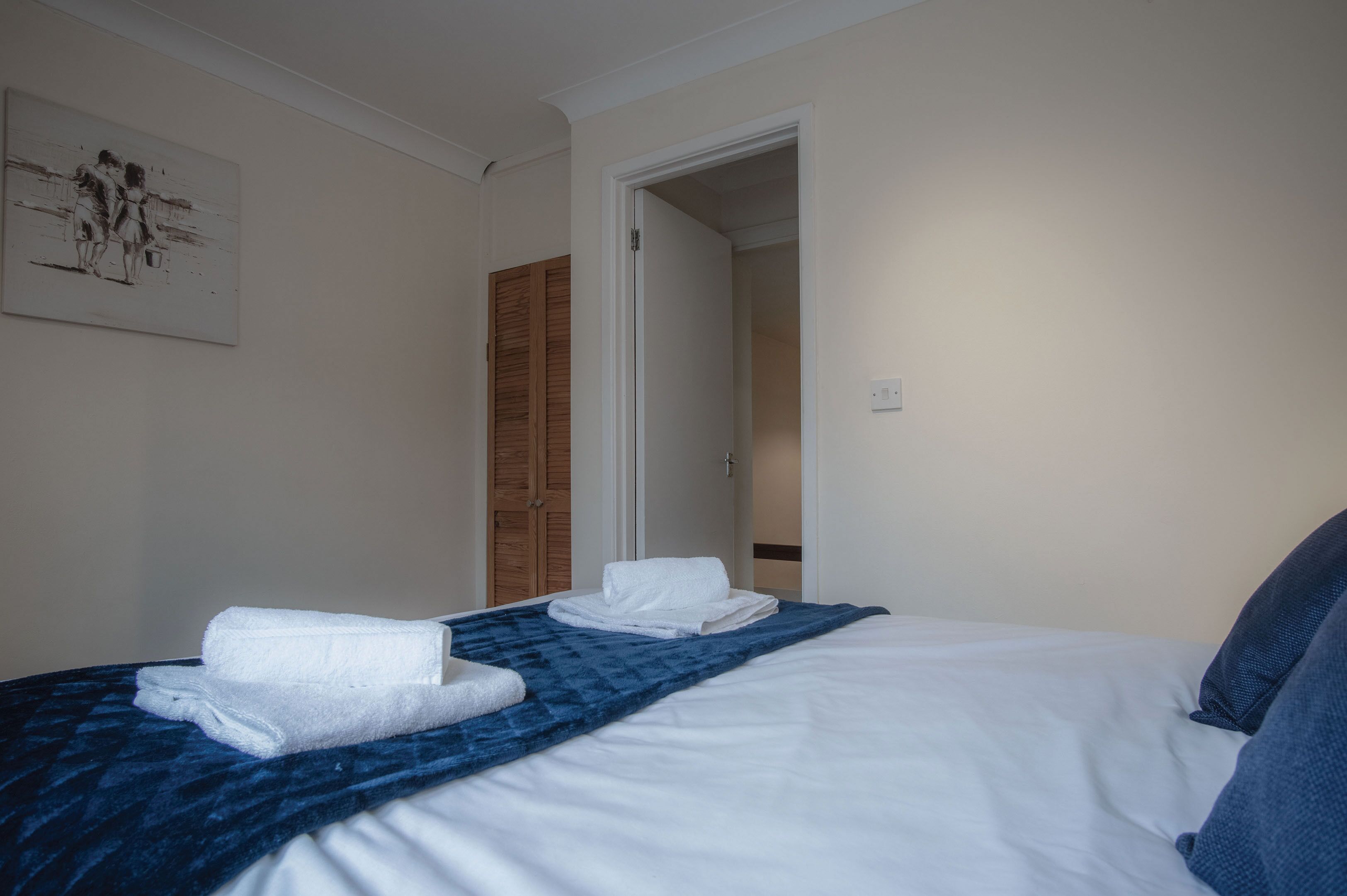 Habitació d'hotel amb un llit, una manta blava i dues tovalloles blanques.