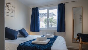 A hotel room with a large bed, a window with curtains, a chair, and a mirror. - Sea Breeze Apt 2 - 2 Bed - Horton Beach (Swansea)