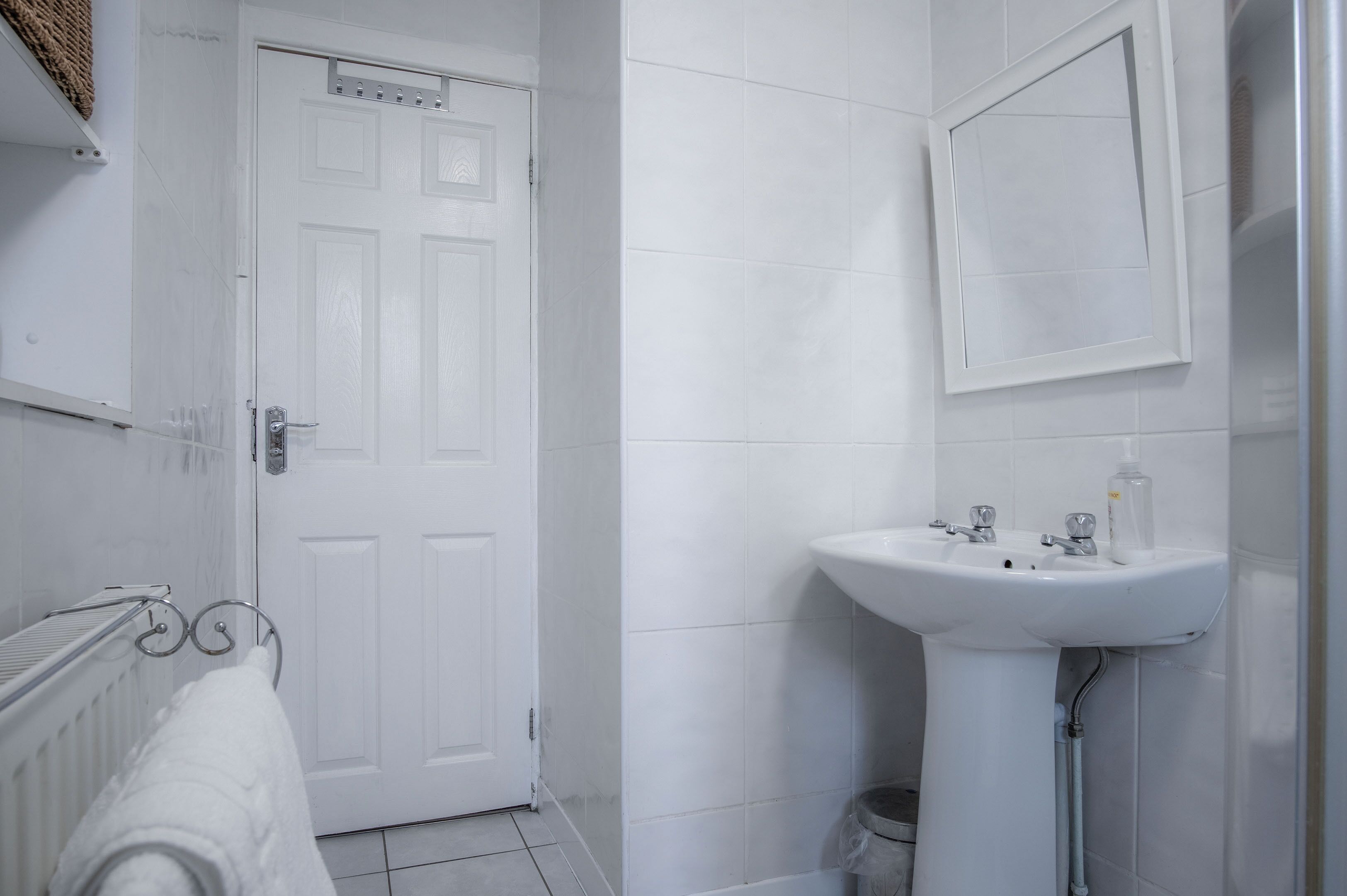 Un baño con una puerta blanca, un lavabo y un perchero para toallas.