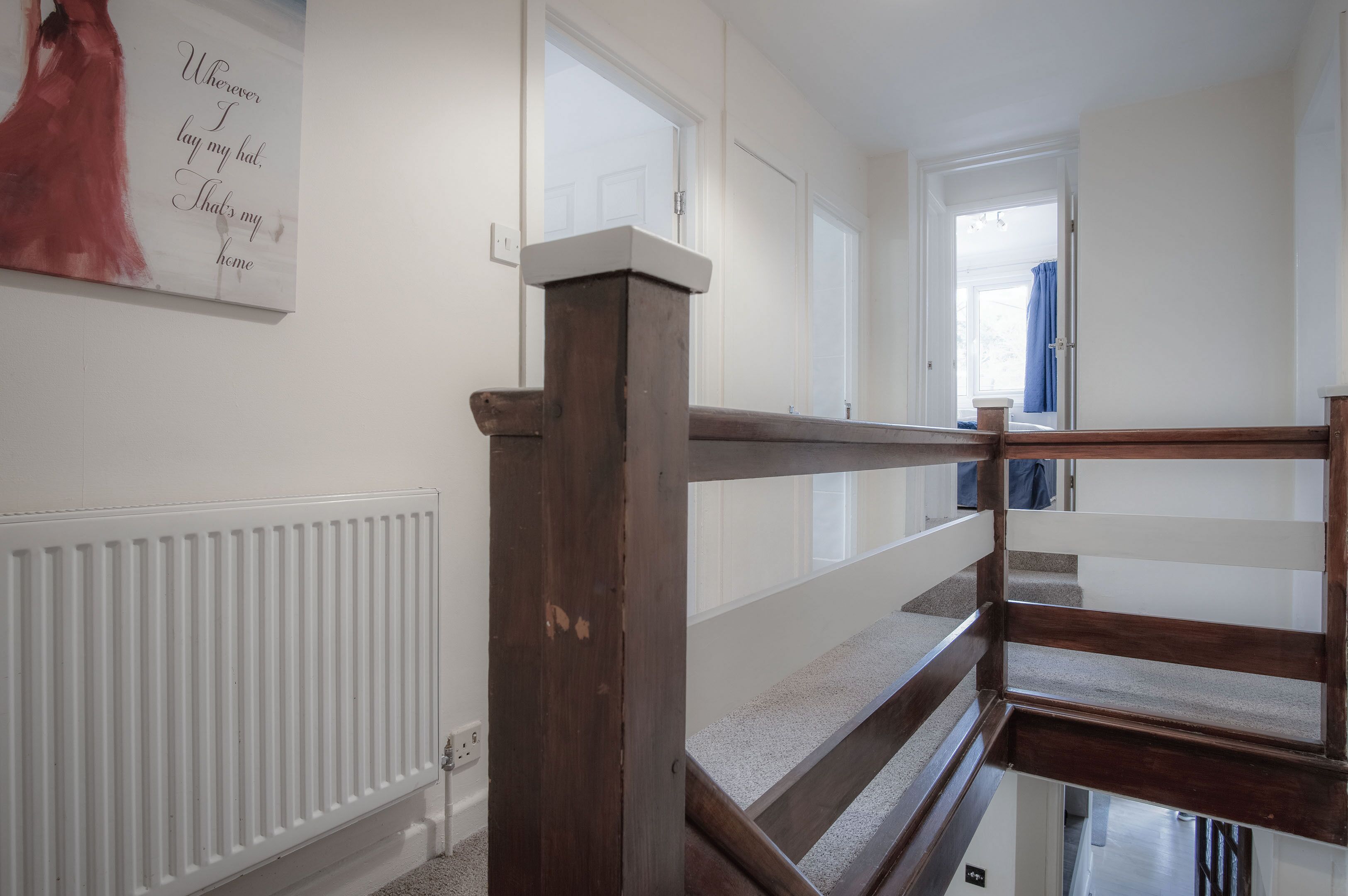 Una scala con ringhiere in legno che conduce a un pianerottolo, pareti bianche e un termosifone.