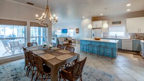 A spacious kitchen with a central island, a dining area with a chandelier, and a view through large windows. - Shore Leave – Relax, Unwind & Enjoy Paradise in Style (Elbow Cay)