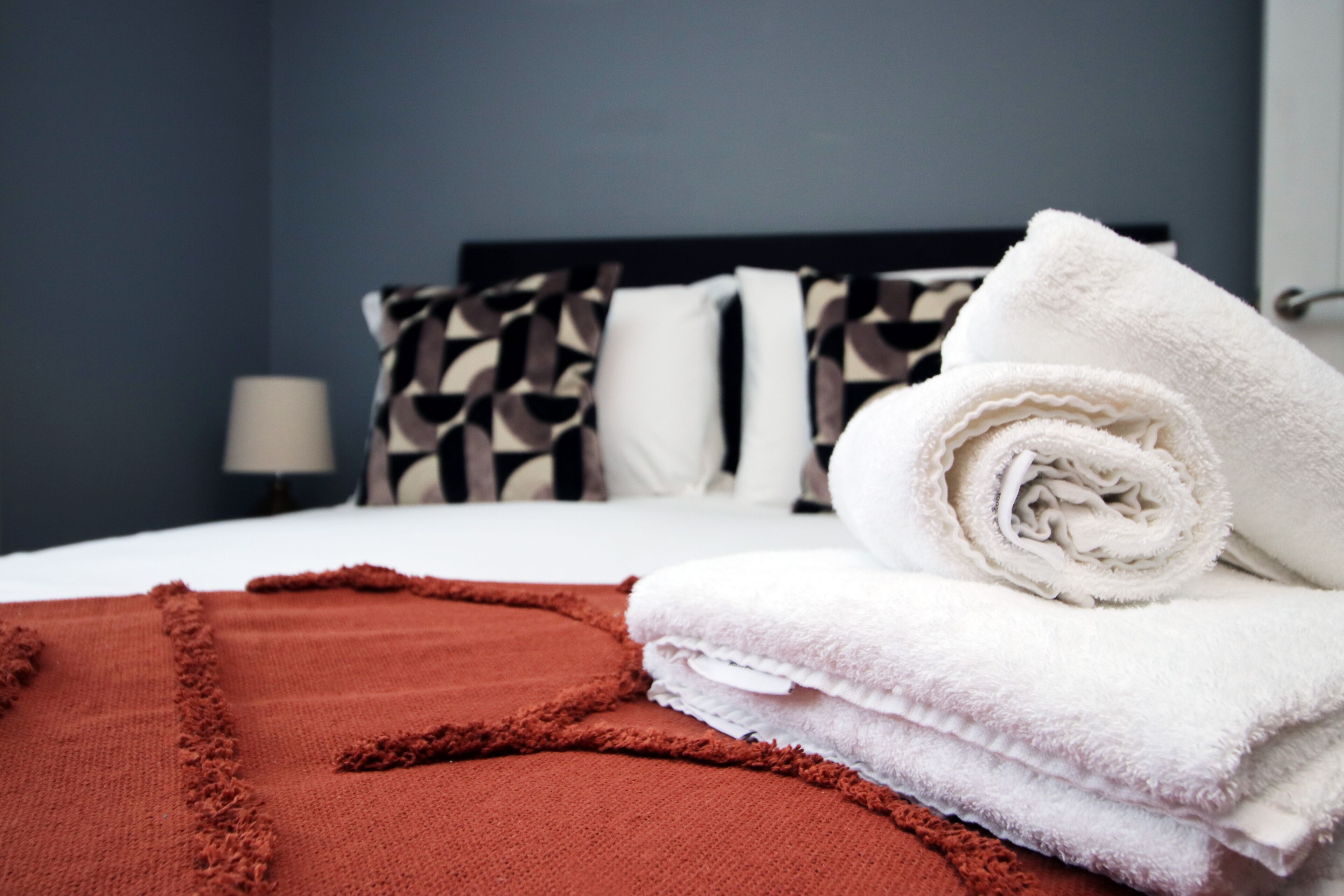 Een net opgemaakt bed met wit en bruin beddengoed, een opgevouwen witte handdoek en een bruin plaid.