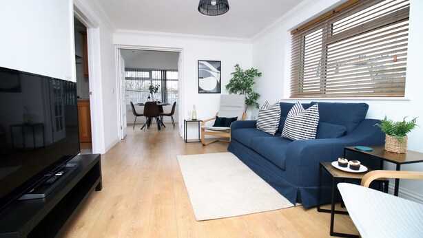 Un salon moderne avec un téléviseur à écran plat, un canapé bleu, une table basse en bois et, au fond, un coin repas.