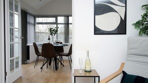 Un coin repas moderne avec une table dressée pour deux personnes, une bouteille de champagne et un verre sur une petite table.