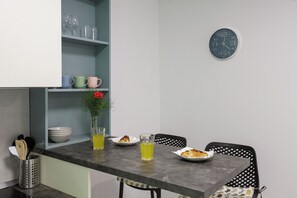 A kitchen with a clock, a dining table with chairs, and a shelf with glassware and bowls. - Beslema comfort one bedroom apartment with balcony and sea view (Dubrovnik)