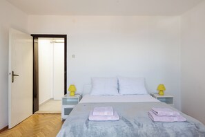 A bedroom with a bed, two bedside tables with lamps, a door, and a hallway. - Beslema comfort one bedroom apartment with balcony and sea view (Dubrovnik)