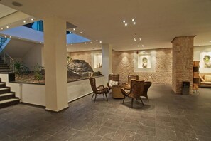A spacious indoor area with a stone wall, a seating area with wicker chairs, and a staircase leading to an upper level. - Ilio Mare Beach Hotel by GHH (Thasos)