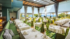 Un restaurante con mesas redondas, sillas verdes y vista al océano.