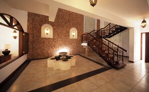 A lobby with a stone wall, a fountain, a staircase, and a wooden railing. - Lantana Galu Beach (Diani Beach)