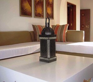 A room with a white table, a decorative lantern, a sofa with striped cushions, and a door in the background. - Lantana Galu Beach (Diani Beach)
