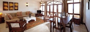 A living room with a sofa, coffee table, TV, and dining area with chairs and a table. - Lantana Galu Beach (Diani Beach)