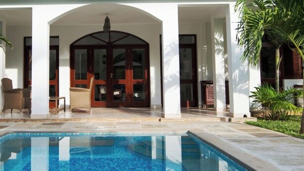 A poolside area with a clear view of the pool, a covered seating area, and a large door leading to the interior. - Lantana Galu Beach (Diani Beach)