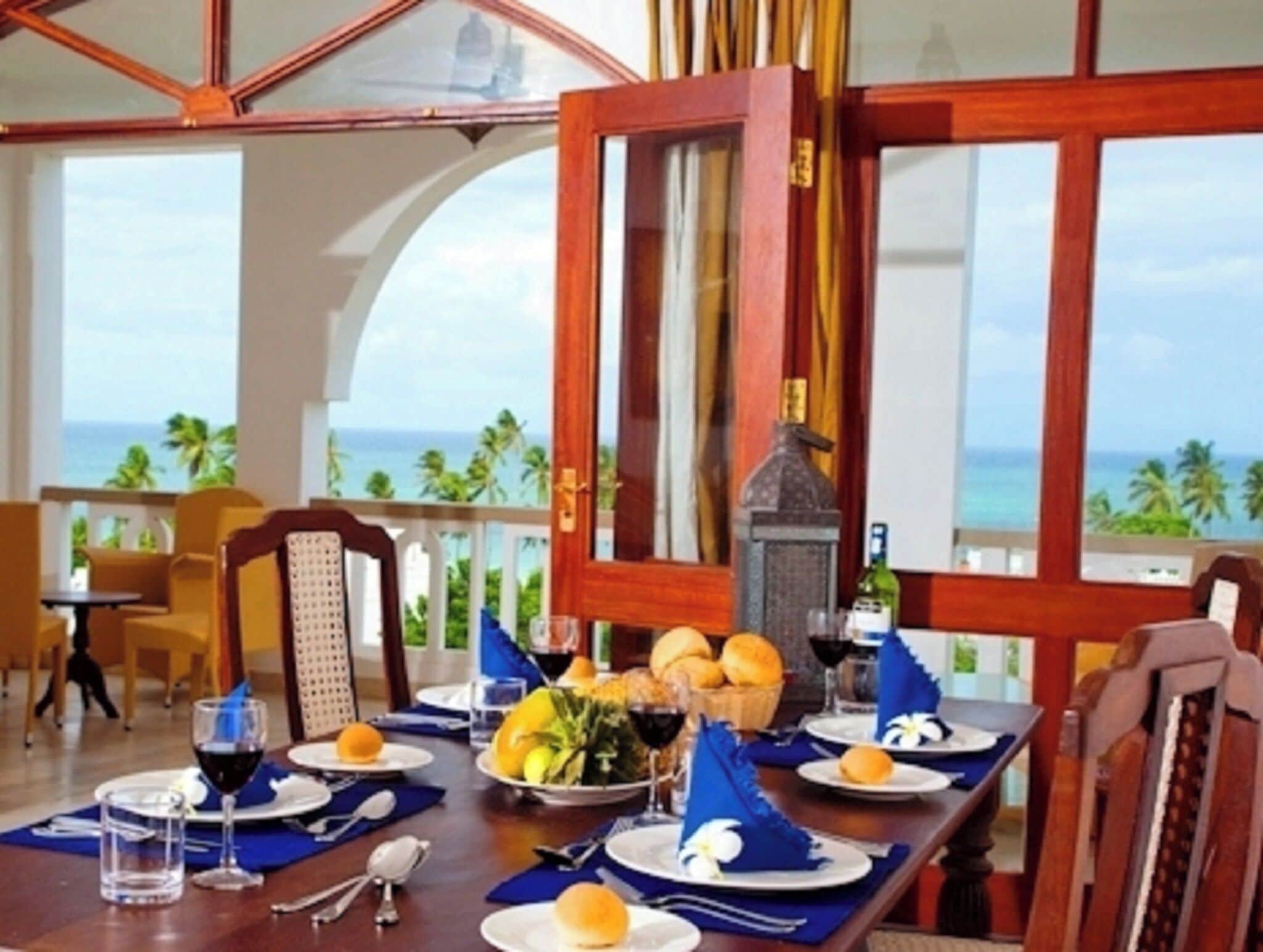 A dining area with a view of the ocean, a table set with plates, glasses, and a bottle.
