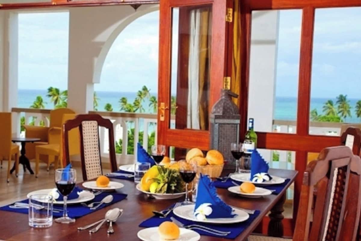 A dining area with a view of the ocean, a table set with plates, glasses, and a bottle.