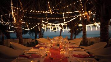A table set for a meal with string lights overhead, palm trees, and a view of the ocean.