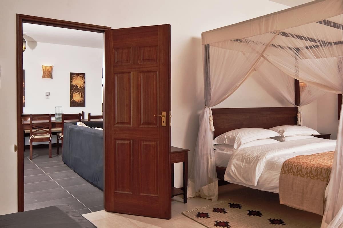 A four-poster bed with a canopy, a wooden door, and a view of the sea.