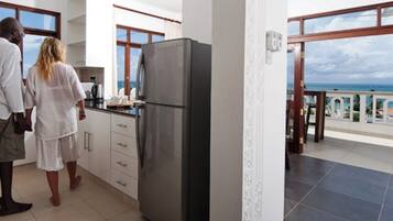 A kitchen with a refrigerator, a window, and a view of the ocean.