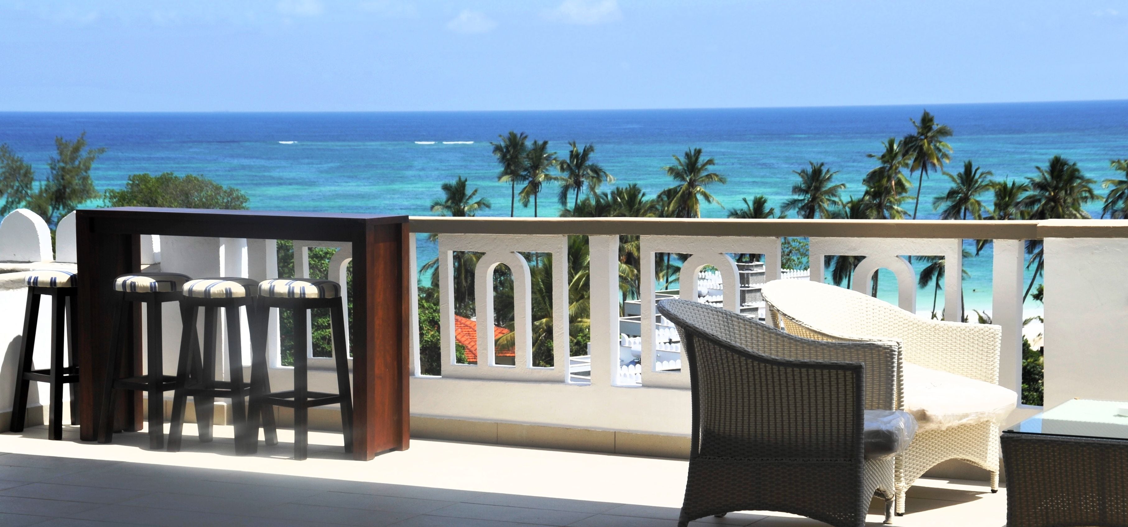 A balcony with wicker furniture, a white railing, and a view of the ocean.