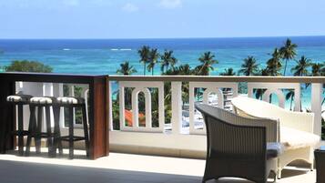A balcony with wicker furniture, a white railing, and a view of the ocean.
