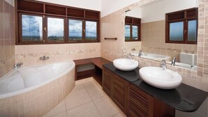 A bathroom with a bathtub, two sinks, a vanity, and large windows with a view. - Lantana Galu Beach (Diani Beach)