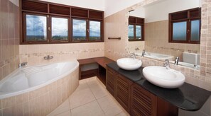 Un baño con bañera, dos lavamanos, tocador y ventanas amplias con vistas.