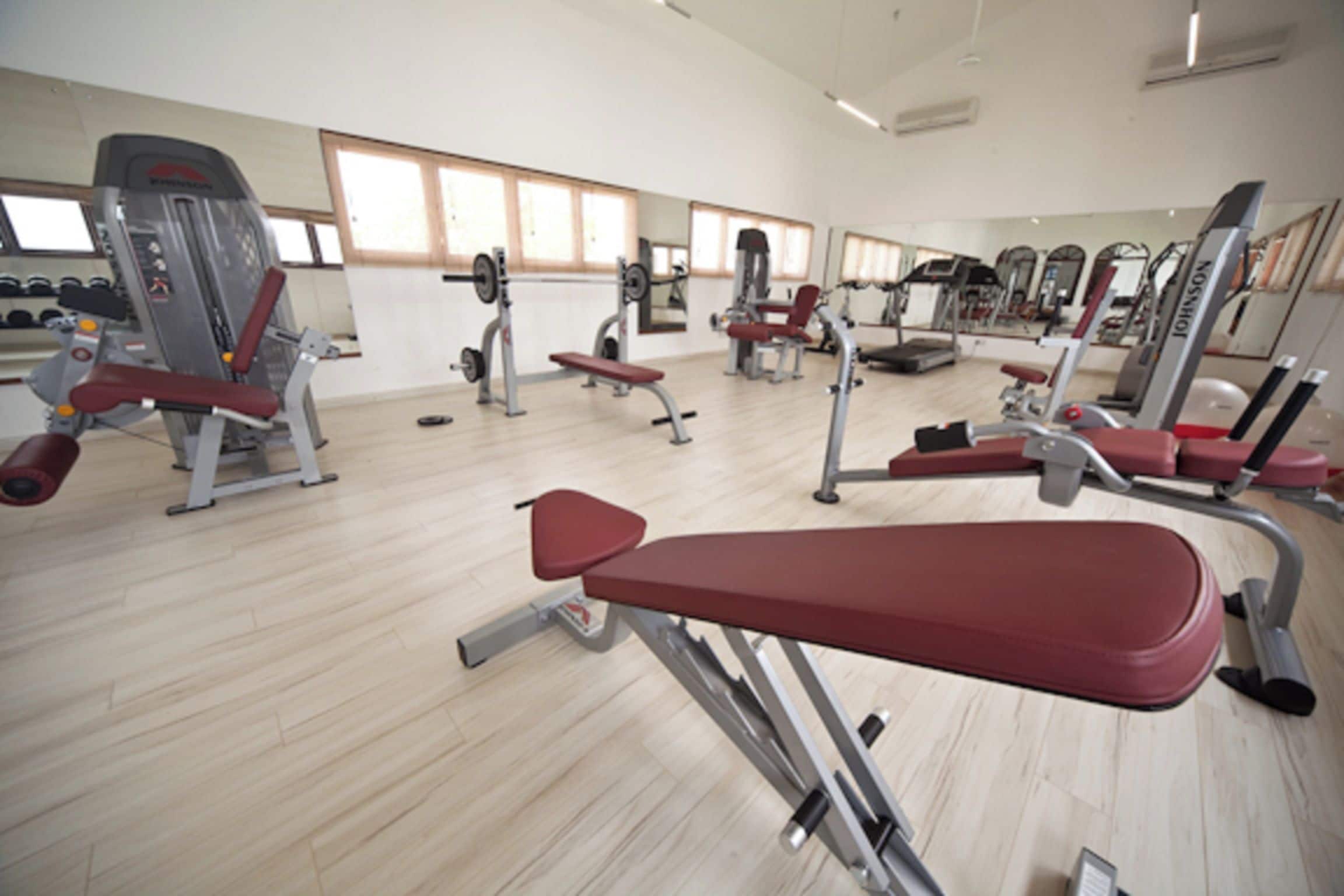 Uma academia com diversos equipamentos de exercício, espelhos e piso de madeira.