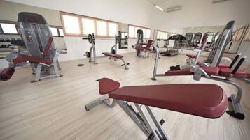 Uma academia com diversos equipamentos de exercício, espelhos e piso de madeira.