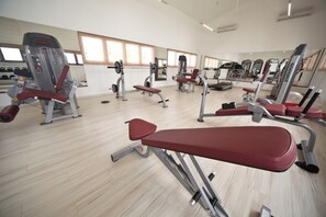 Un gimnasio con diversas máquinas de ejercicio, espejos y suelo de madera.