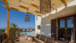 A wooden outdoor dining area with a pool in the background. - EcoHome Villa (Chania)