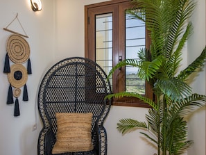 Relax in a serene space with a woven chair, wall hanging, and lush greenery.