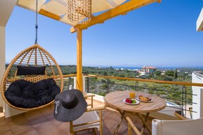 A balcony with a hanging chair, a table with plates of food, and a view of the landscape. - EcoHome Villa (Chania)