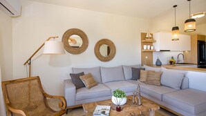 A modern living room with a light grey sofa, a wooden coffee table with a magazine, a wicker chair, and two wall-mounted mirrors. - EcoHome Villa (Chania)