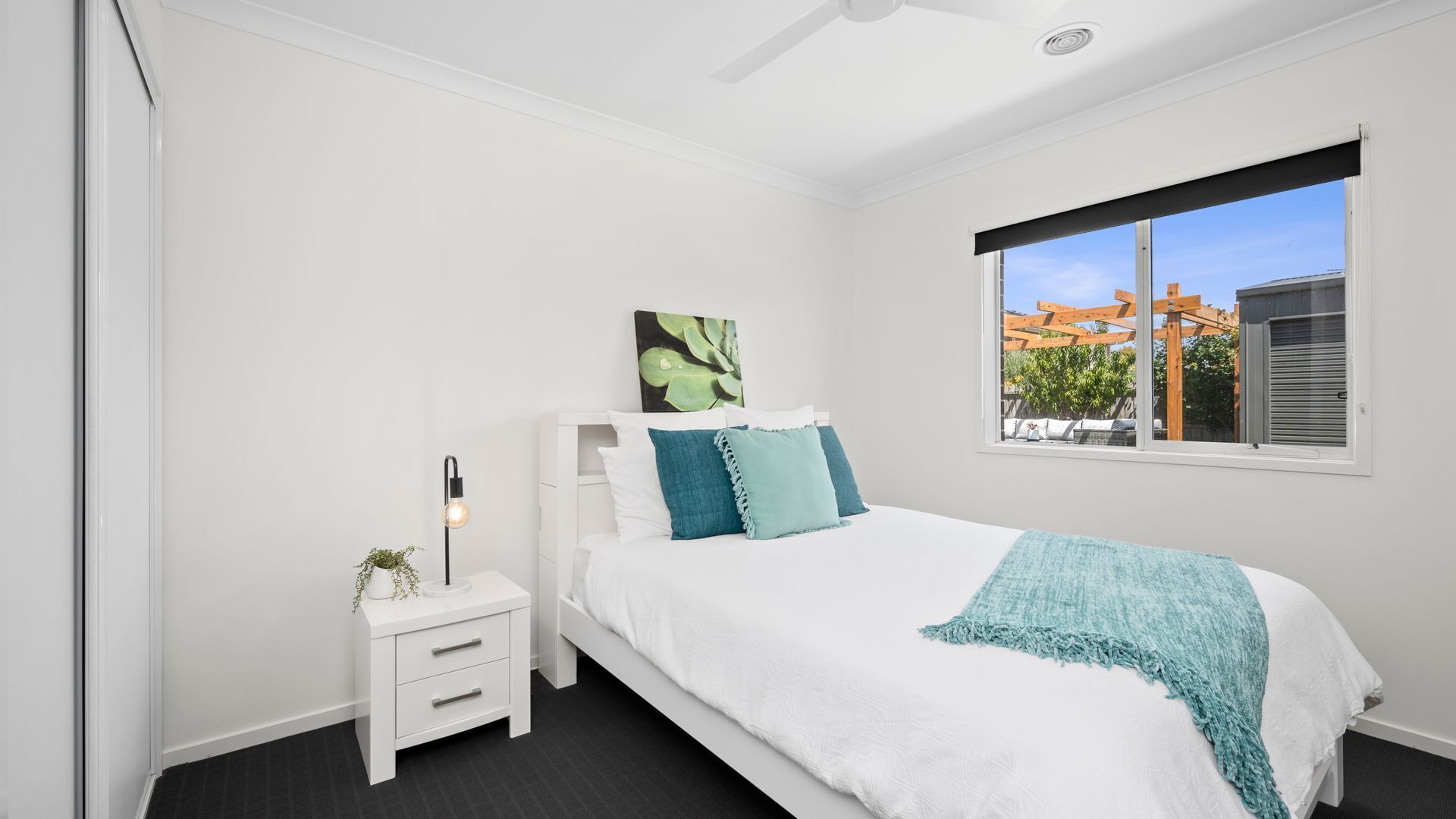 A bedroom with a bed, a nightstand, a floor lamp, and a window with a view of buildings.