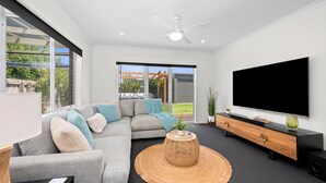 A modern living room with a sectional sofa, a flat-screen TV, and a ceiling fan. - Aerial Beach House - Beach & Golf (Torquay)