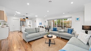 A modern living room with grey sofas, a round coffee table, and a dining area with a table and chairs. - Aerial Beach House - Beach & Golf (Torquay)