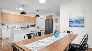 A modern kitchen with wooden cabinets, a central island, and pendant lighting. - Aerial Beach House - Beach & Golf (Torquay)