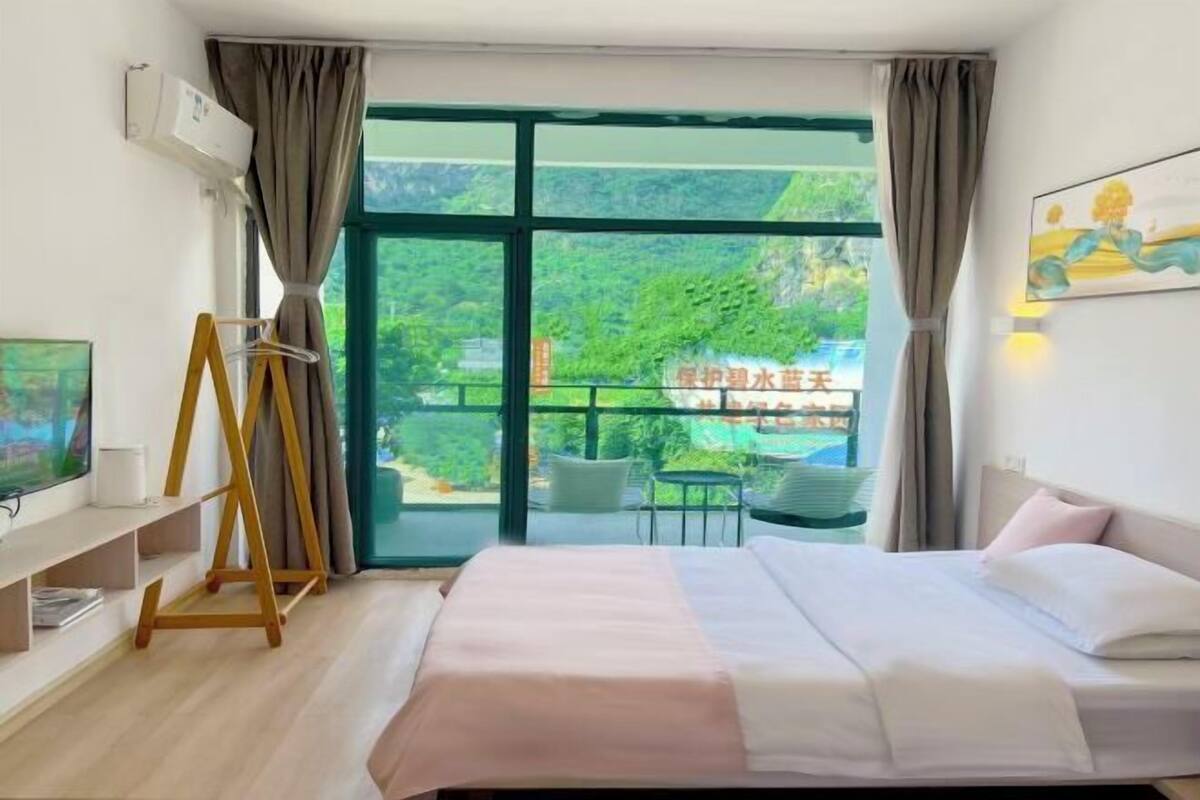 Une chambre d’hôtel avec un lit, une télévision, un cintre en bois et une vue sur la verdure.