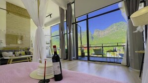 A modern hotel room with a large balcony, a bed with a pink bedspread, a wine bottle, and a cake on the table. - Yangshuo Xitian Yueshan Homestay (Eternal Love Store) (Yangshuo)