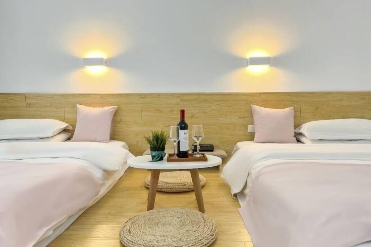 Une chambre d’hôtel avec deux lits, une petite table ronde sur laquelle se trouvent une bouteille et des verres, et deux lampes fixées au mur.