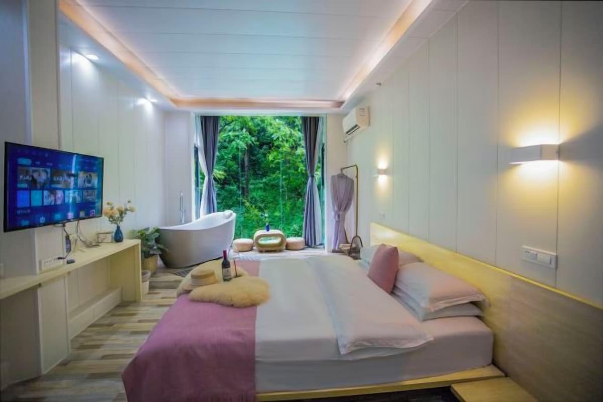 Une chambre à coucher moderne avec un lit, une télévision, une baignoire et une fenêtre avec des rideaux.