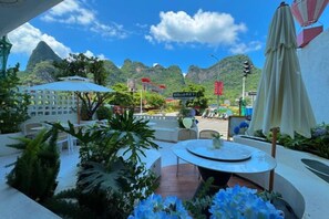 Un espace extérieur aménagé avec une table et des chaises, entouré de plantes et de parasols, offrant une vue sur un paysage montagneux.